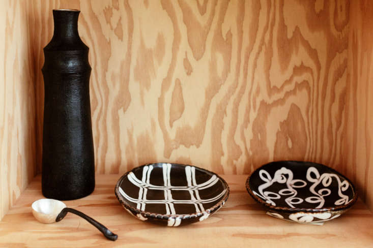 Open plywood shelving containing vases and bowls, serving as shared storage between different zones.