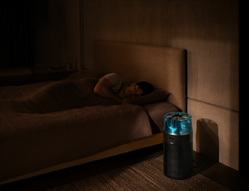 A Dyson air purifier operating quietly next to a bed in a dark, peaceful bedroom.