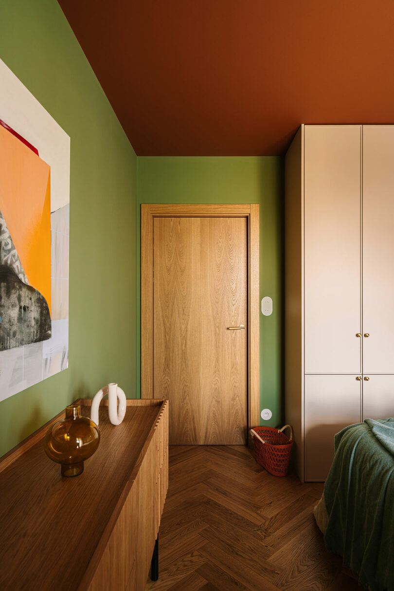 Bedroom with deep green walls, a light wood door, and a striking terracotta-hued ceiling.