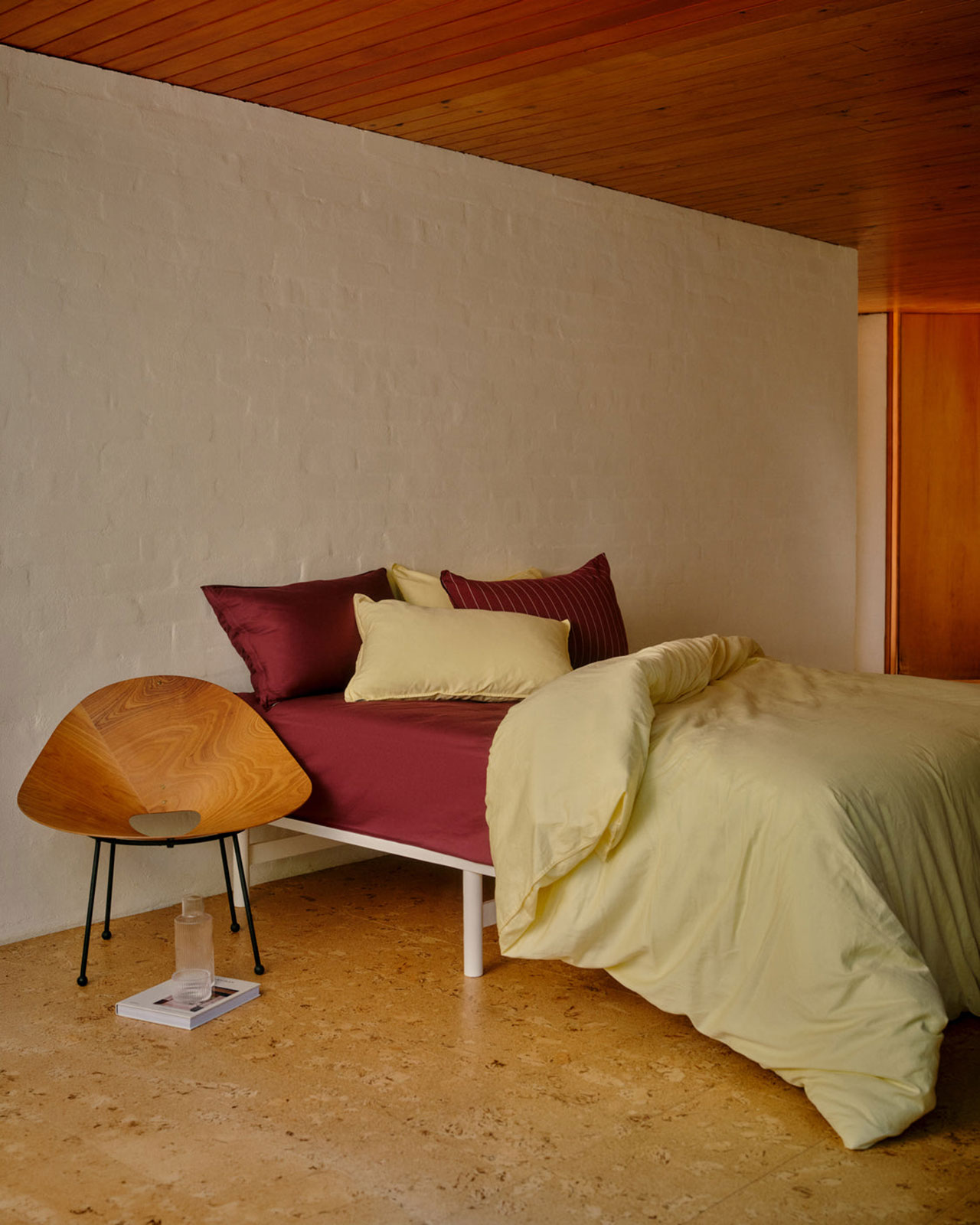 Layered organic bedding in burgundy and pale yellow on a neatly made bed.