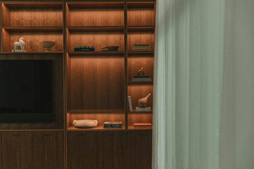 Wooden shelves with integrated warm LED lighting displaying books and sculptures.