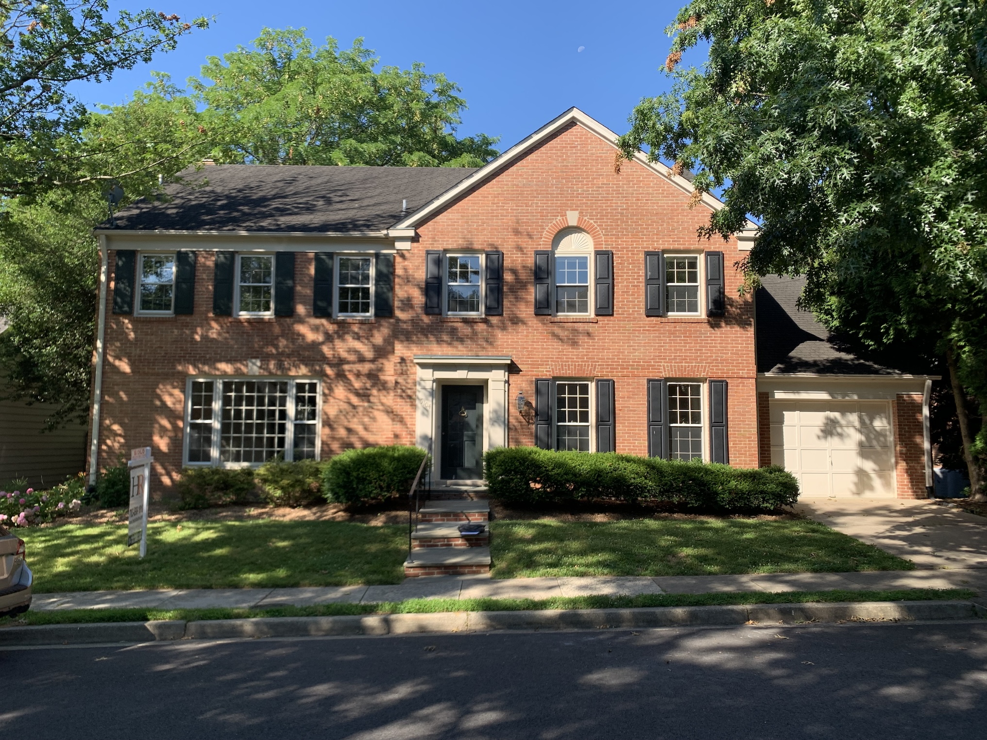 A traditional 1980s red brick colonial house with black shutters and a white door.