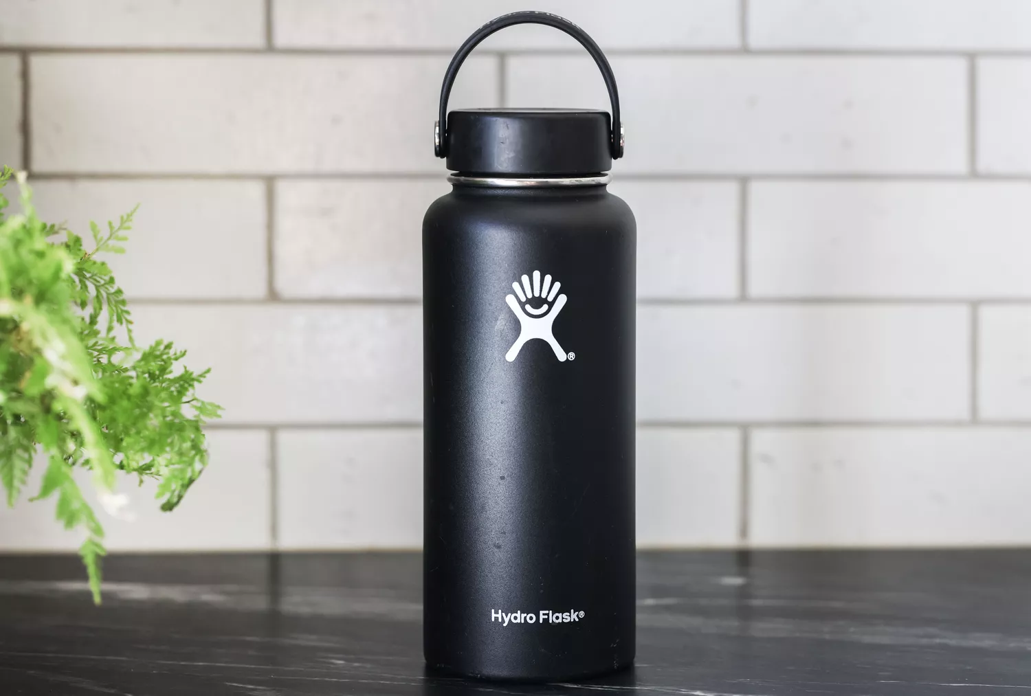 A matte black reusable water bottle sitting on a clean marble kitchen countertop.