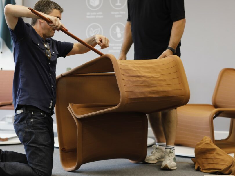 Two people assembling the brown fabric sleeve onto the metal frame of an Isomi Knit One chair.