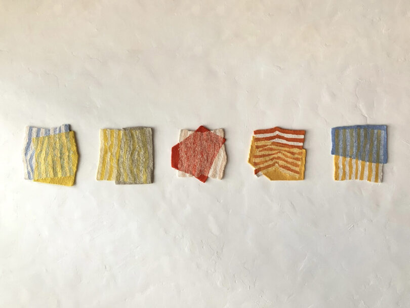 Five square fabric swatches in various colors and striped patterns displayed on a minimalist wall.