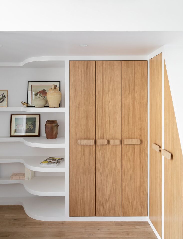 A minimalist studio interior featuring curved plaster walls and integrated light oak storage units.