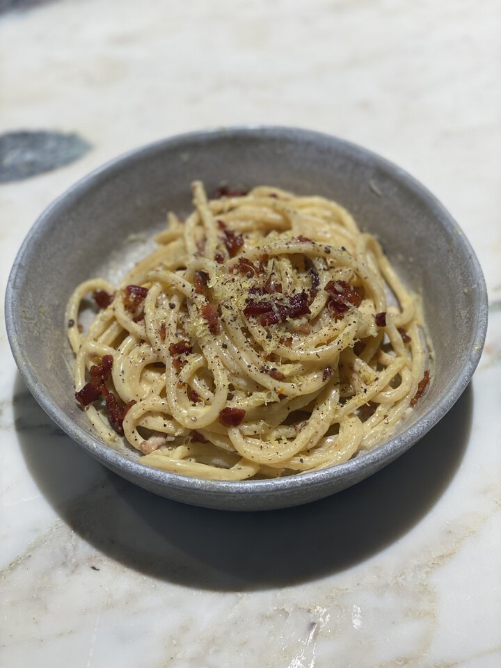 A serving of bucatini carbonara finished with lemon zest and fresh herbs.