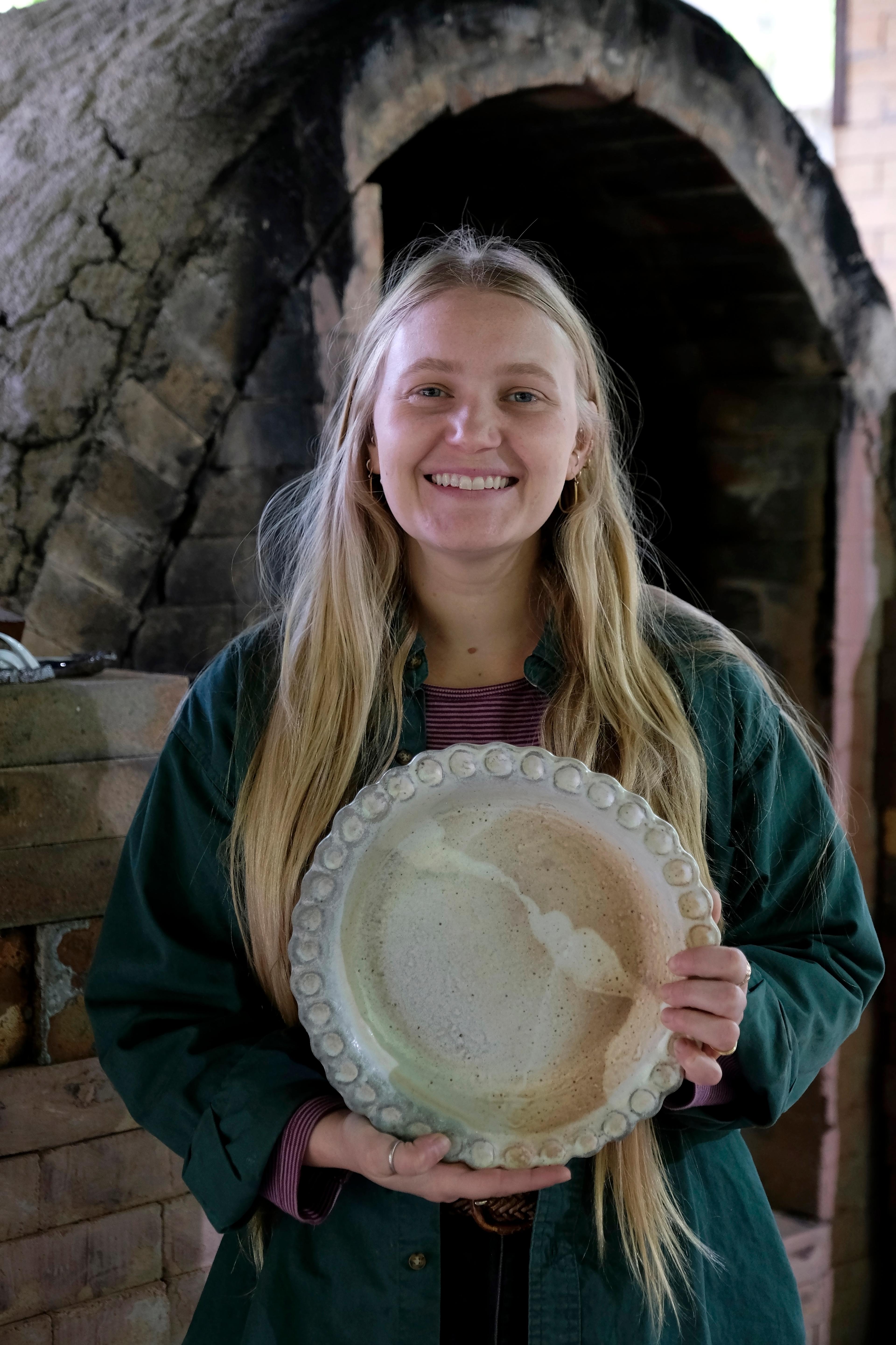 Artist Meghan Burke smiling while holding a large, finished wood-fired ceramic pie plate.