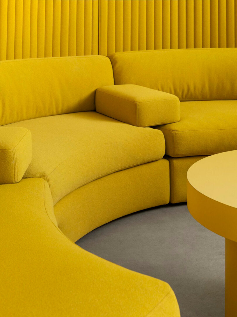 Yellow curved sofa with matching armrest set against a vertically paneled yellow wall.