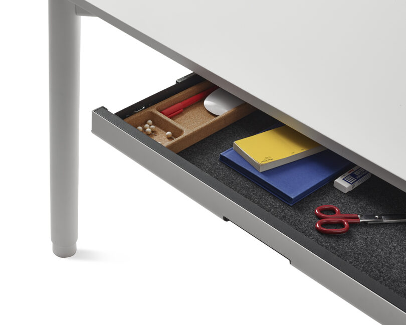 Close-up of an open under-desk drawer on a wooden desk with neatly organized office supplies.