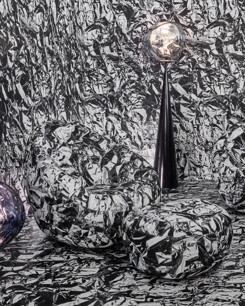 A futuristic room setup where the chair, ottoman, and walls are all covered in highly reflective crinkled silver material.