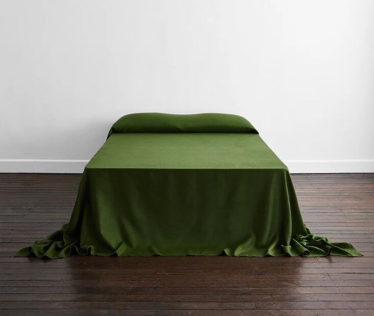 An olive-green heavy linen bed cover made from French flax, showing its soft, heavy drape over the sides of a bed.