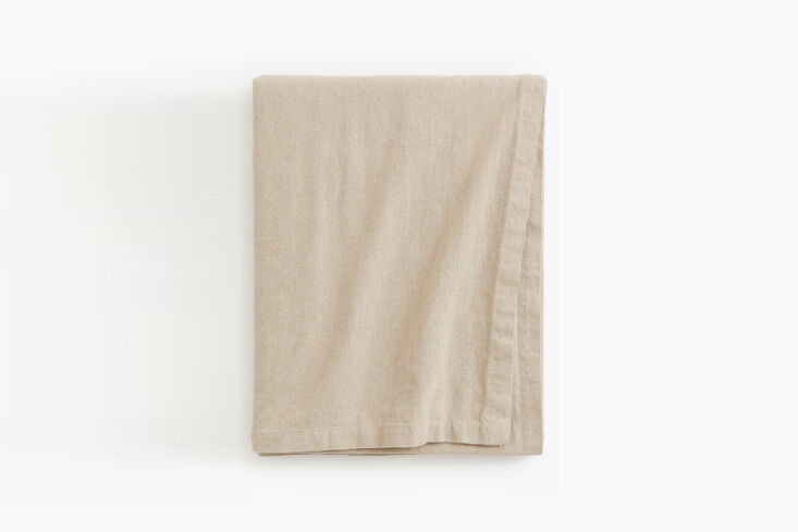 Close-up of a wrinkled, light-colored washed linen tablecloth on a dark wood table.