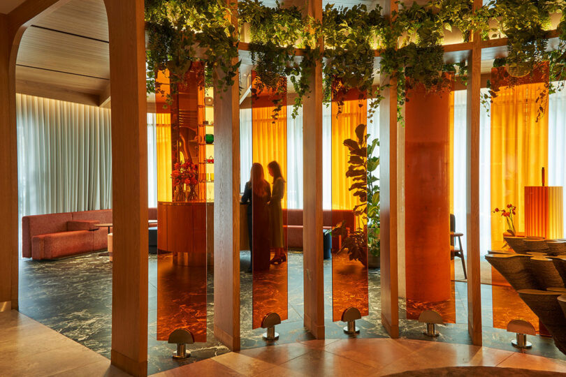 Tall illuminated structure with hanging greenery in the center of a lounge area.