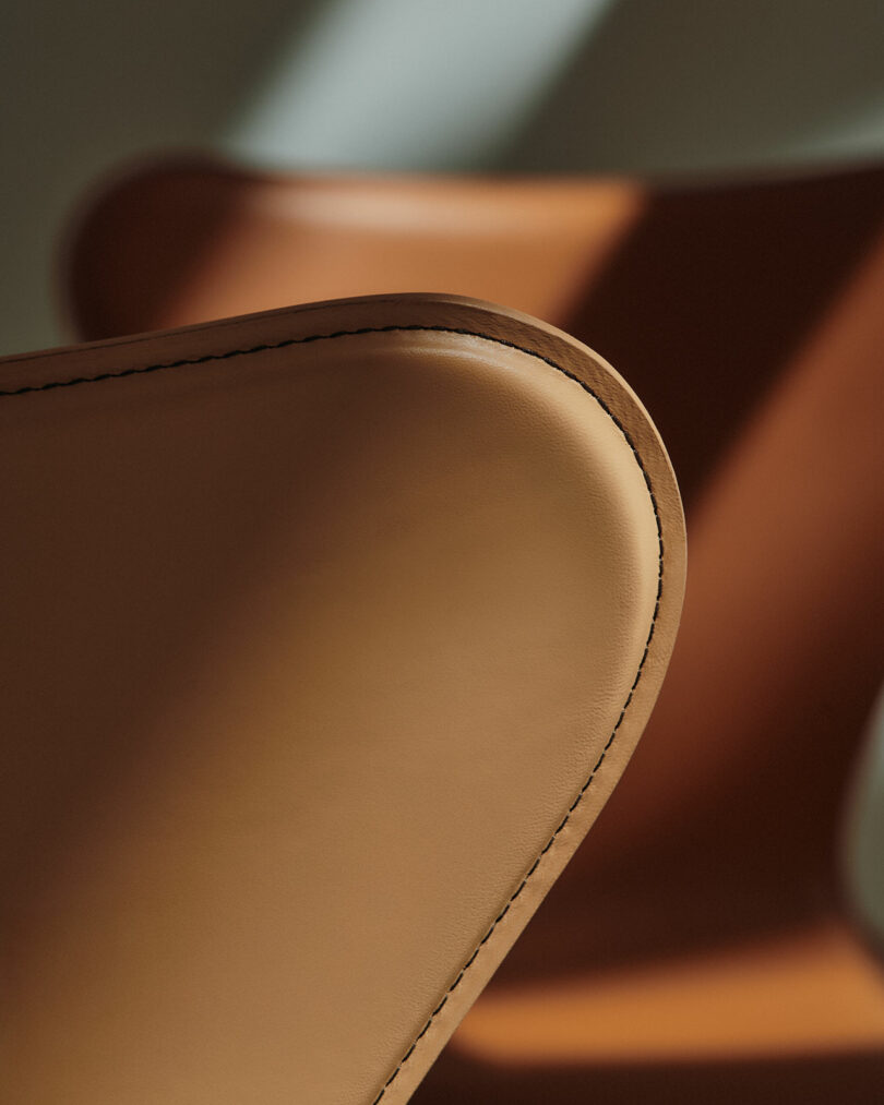 Extreme close-up of tan leather upholstery with visible white stitching on the curved edge of a Series 7 chair.