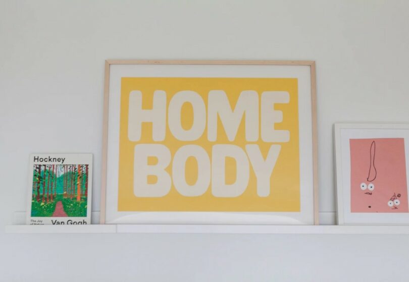 A styled shelf with a 'HOME BODY' print, yellow and white lettering, and colorful art books.