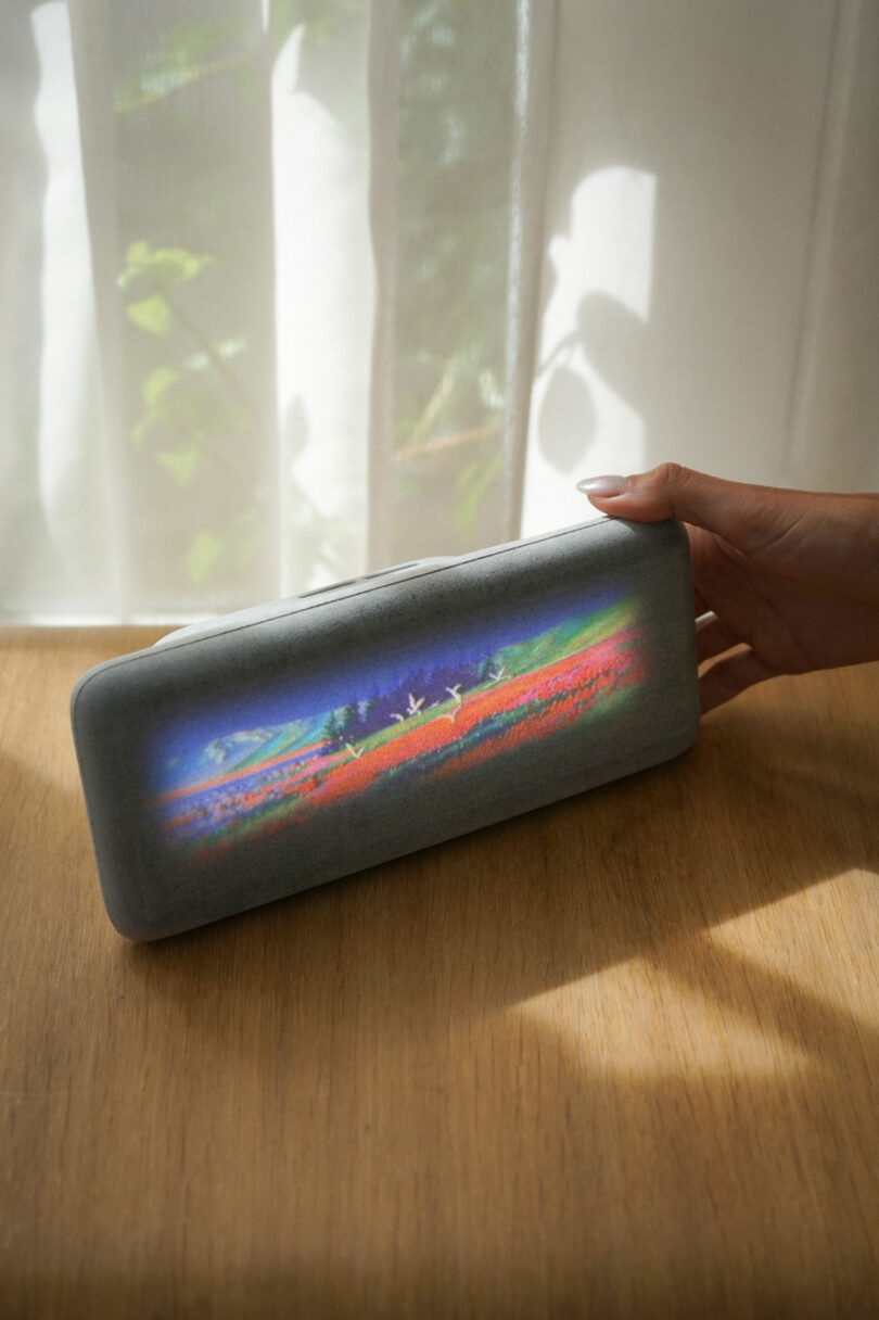 The gray Dream Recorder device on a wooden table displaying a colorful landscape.