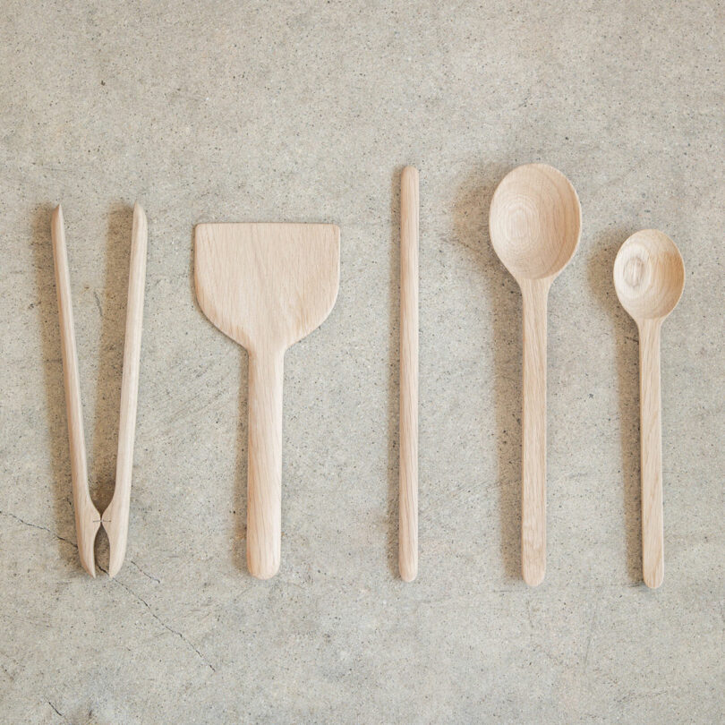 Five white oak kitchen utensils including spoons and spatulas arranged neatly on a light surface.