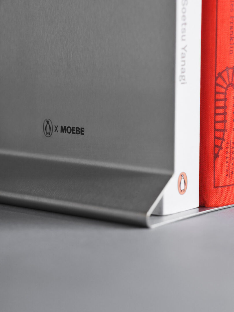 Macro shot of the X MOEBE branding on the powder-coated steel surface of the bookstand.