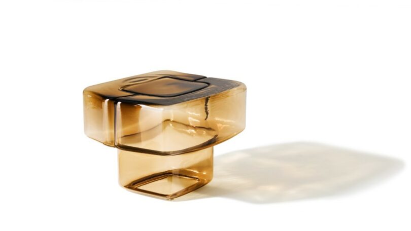 An amber glass cube-shaped table with a hollow rectangular base and smooth rounded edges.