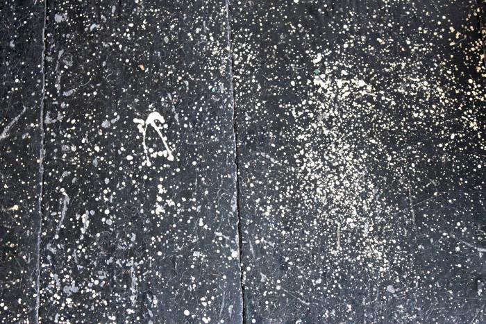 Close-up of a hand flicking a brush to create elongated paint drips on a floor surface.