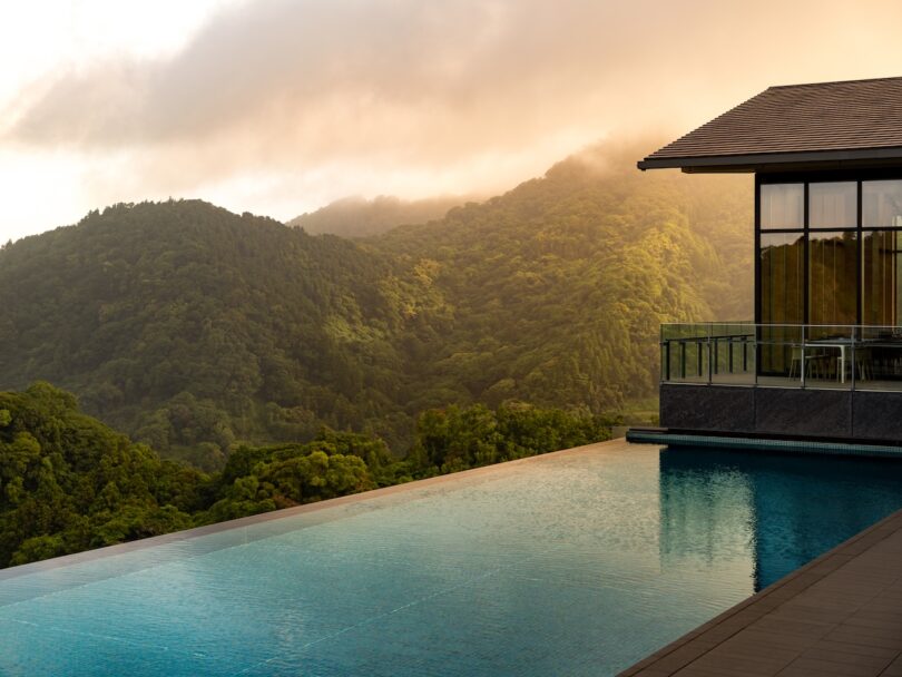 An infinity pool at sunset overlooking lush green forested hills in Japan.