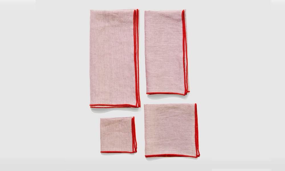 Oyster colored napkins with red contrast stitching arranged on a table.