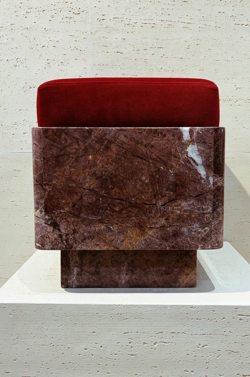 A minimalist red velvet cushion positioned atop a heavy, rectangular brown marble base.