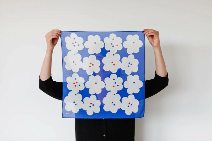 A person holding a blue cloth featuring white floral patterns with multicolored centers.