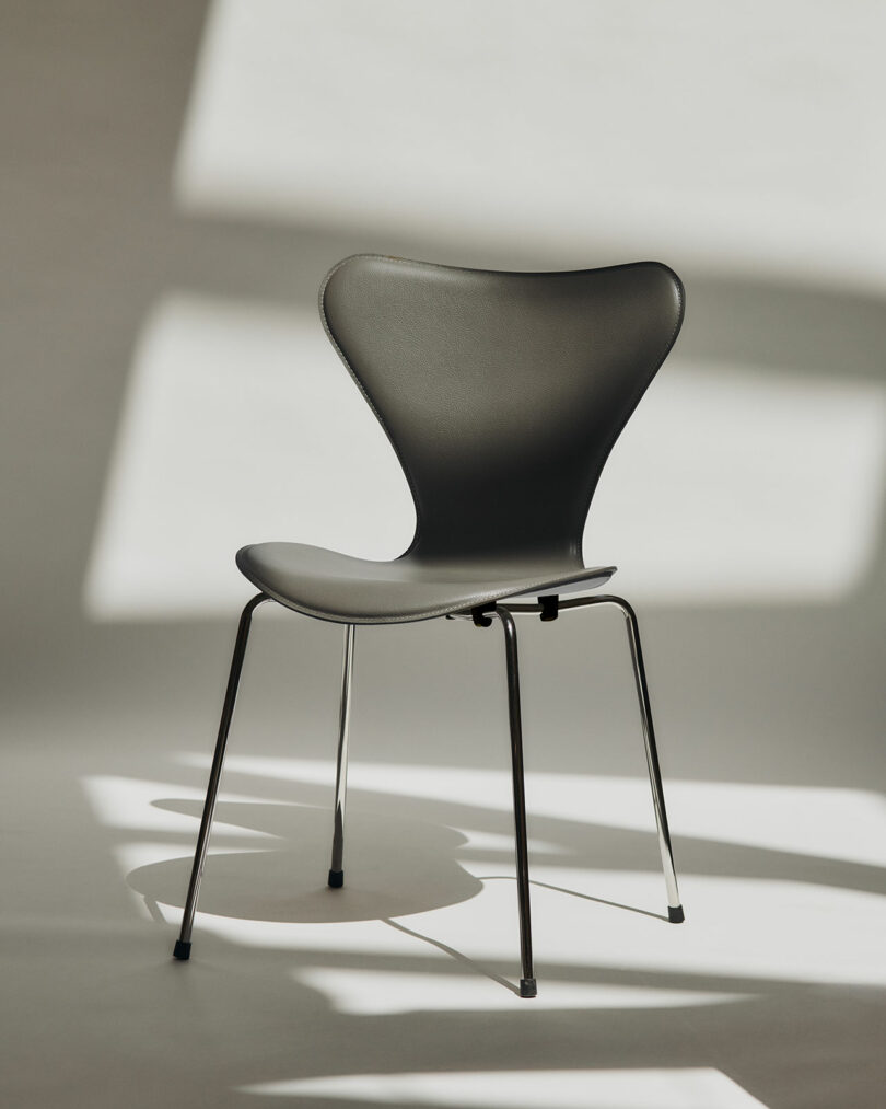 Side profile of a black Series 7 chair showing its iconic curved backrest and metal legs against a shadow-patterned background.