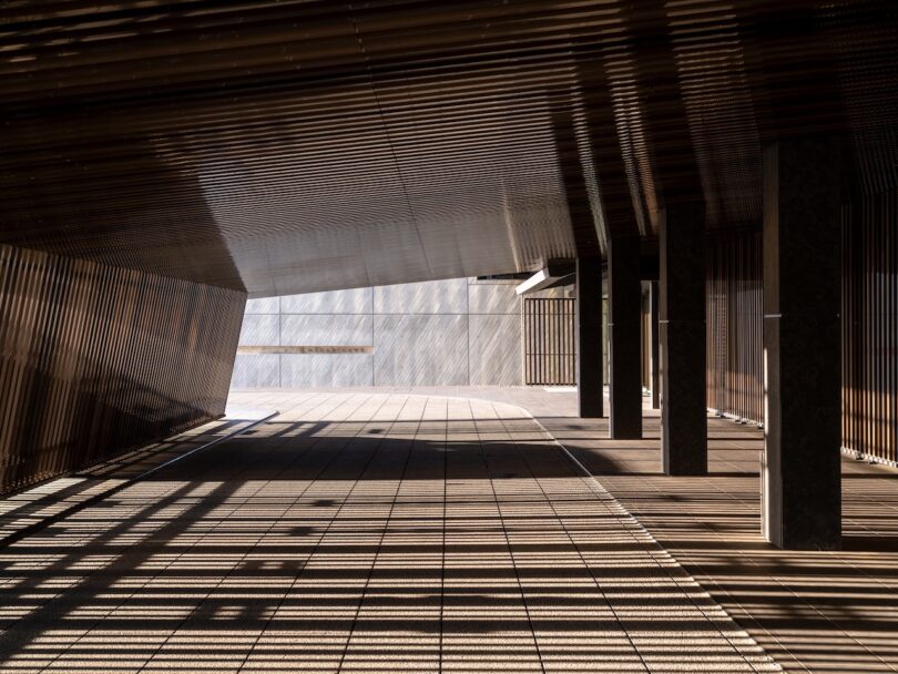 Geometric shadow patterns cast by a slatted architectural overhang onto a modern tiled walkway.