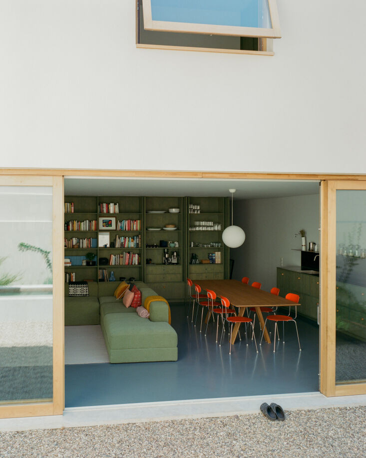 Looking from the pebbled courtyard into the living room featuring orange Enzo Mari chairs.