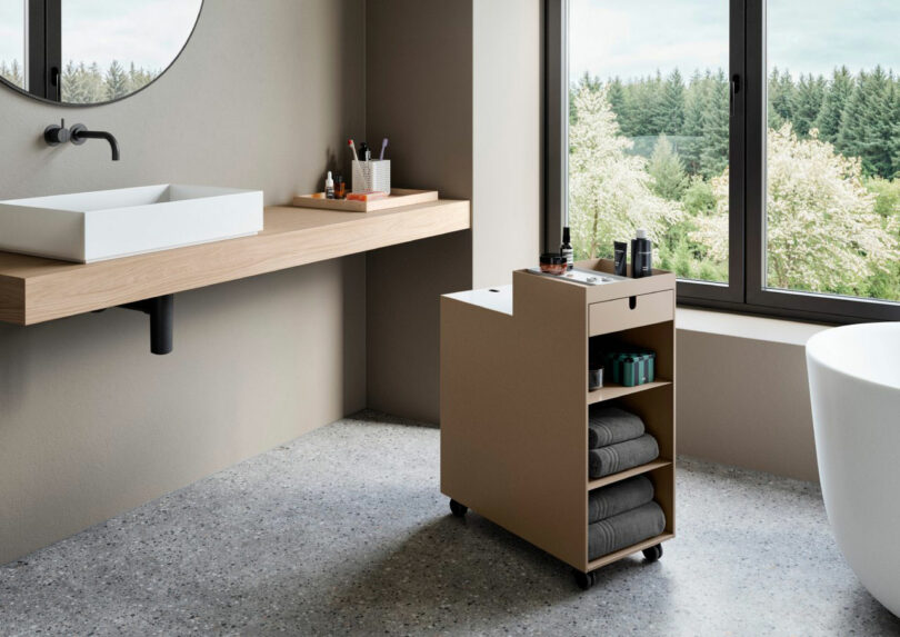 A white mobile storage unit holding towels and toiletries in a modern bathroom.