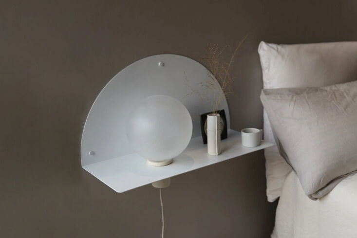 A half-moon shaped wooden shelf with a sphere light on a dark wall.