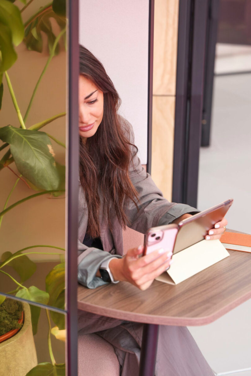A woman working intently on a tablet and smartphone inside a quiet, modern workspace.