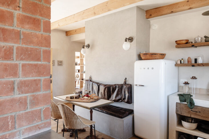 A small dining banquette with chocolate leather cushions and a compact Smeg refrigerator.