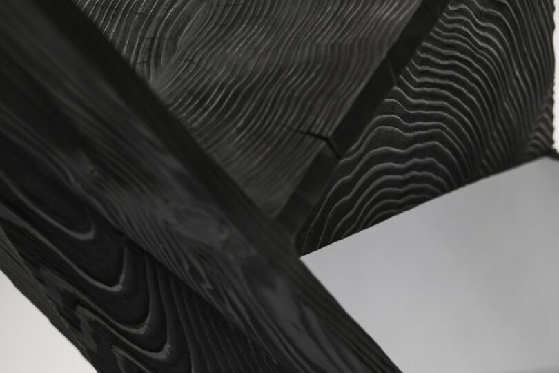 Close-up of blackened wooden beams intersecting at sharp geometric angles.