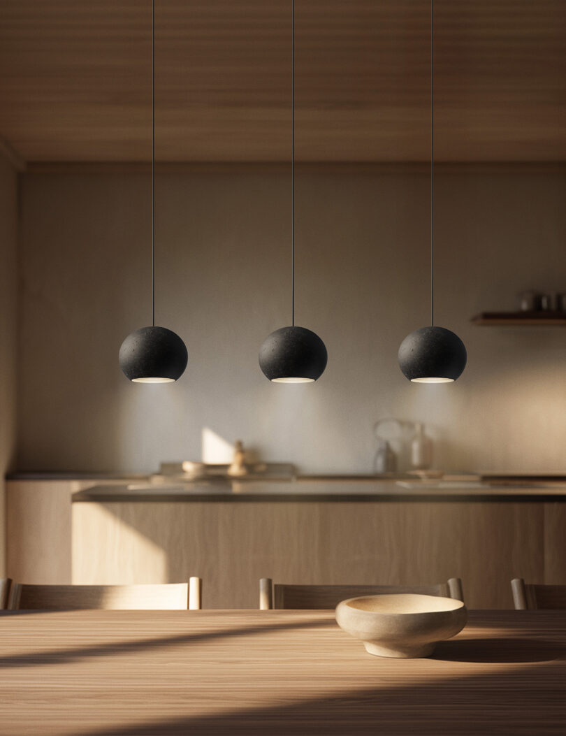Three black Foscarini pendant lights hanging over a natural wood dining table in a minimalist kitchen.
