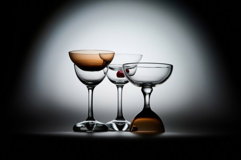 Three different handblown cocktail glasses arranged together, including one with a cherry and two with amber tints.