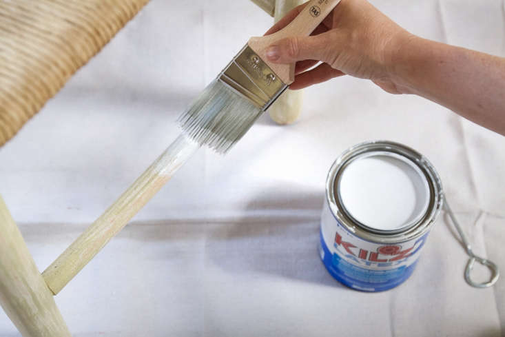 A wooden chair part being coated with white primer to block old stains.