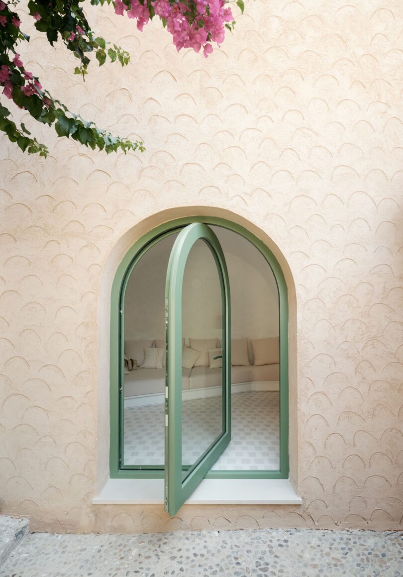An arched window with a green frame set against a beige lime mortar wall.