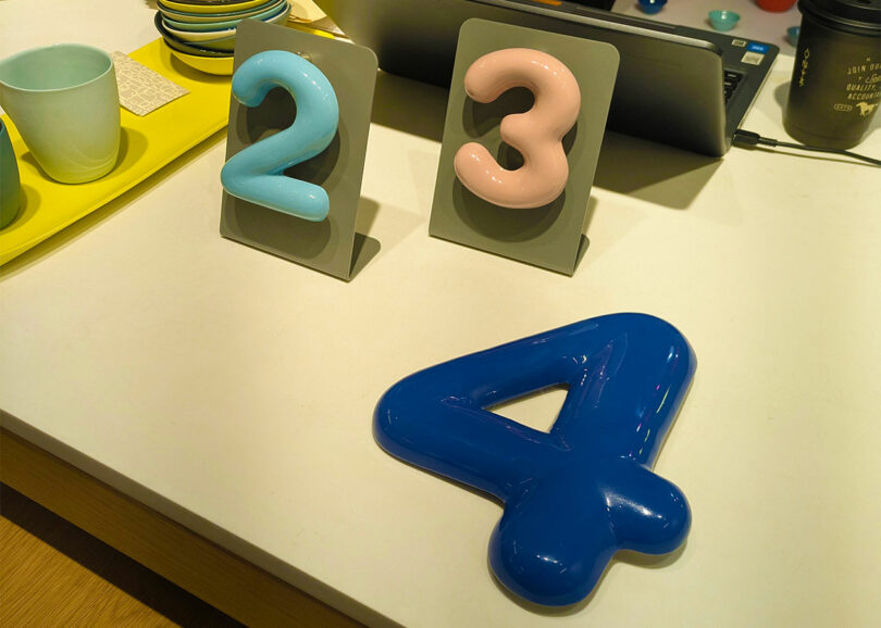 Large blue and pink plastic numbers 2, 3, and 4 displayed near modern ceramic plates.