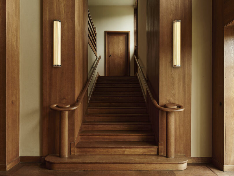 Wood-paneled staircase flanked by two vertical wall lights leading to a door.
