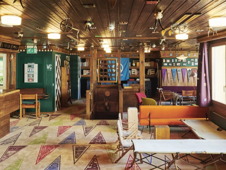 A hotel lobby featuring a custom carpet with colorful mountain flag motifs and vintage wooden furniture.