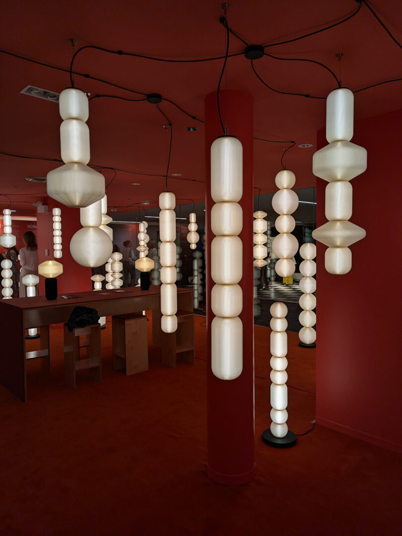 A red-themed installation with cylindrical pendant lights and modern furniture in a bold exhibition space.