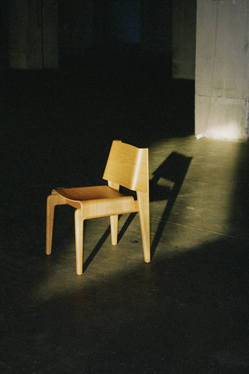The wooden chair standing alone under a spotlight, casting a sharp shadow on a concrete floor.
