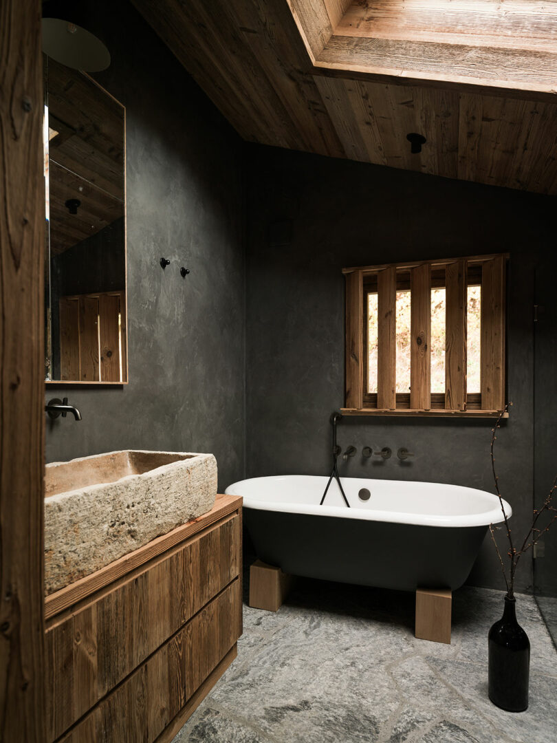 A modern bathroom with a stone sink, slate flooring, and a freestanding tub under a skylight.