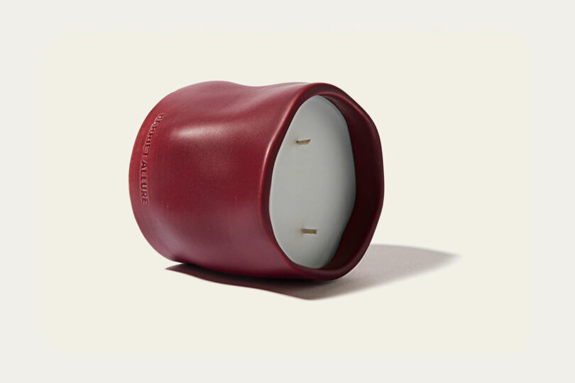 An irregularly shaped red sculptural candle holder with a white candle.