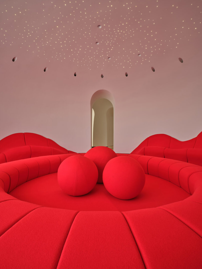 A modern interior with curved red seating and a ceiling featuring many small, recessed lights.
