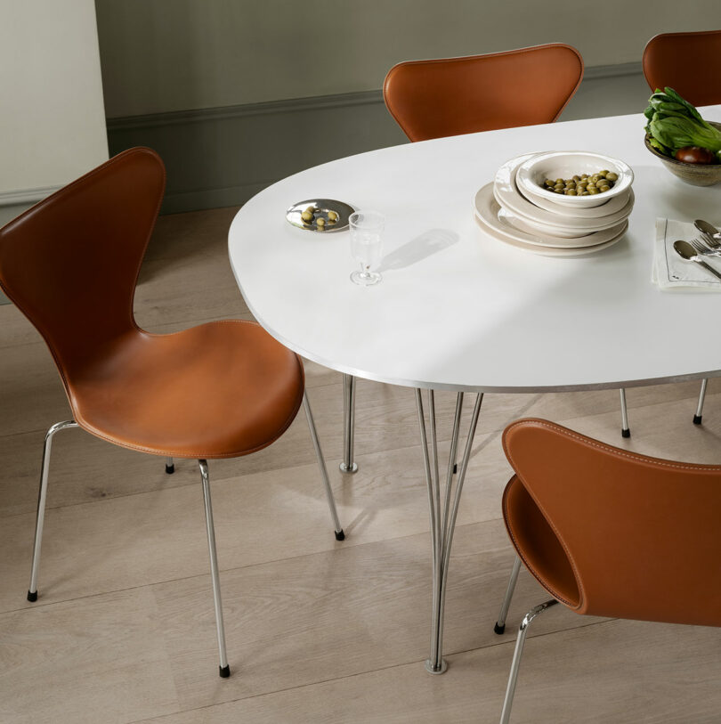 A modern dining room featuring a white oval table paired with brown leather Series 7 chairs.
